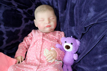 A baby doll resting on a soft purple blanket, showcasing its delicate features and bright clothing.